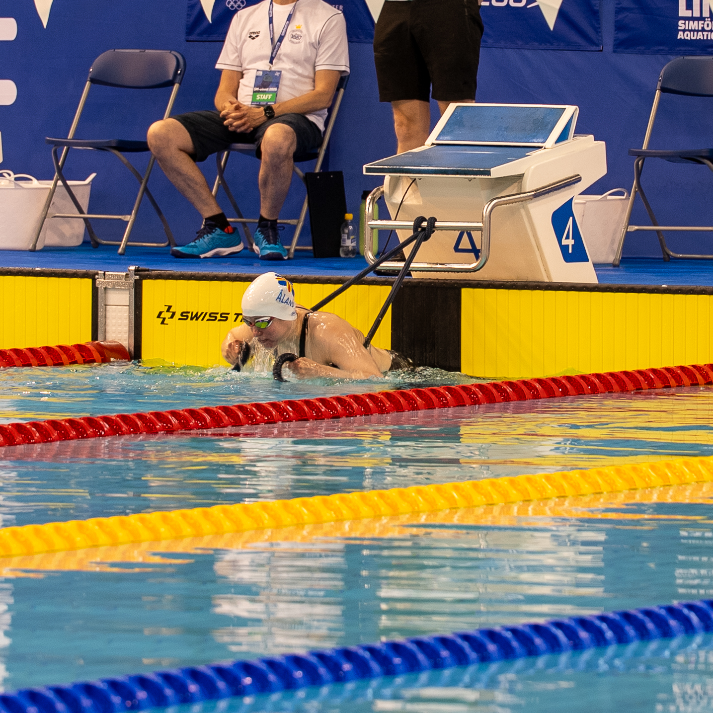 Kuvassa henkilö lähdössä uimaan kilpailussa altaan päädystä käyttäen narua apuvälineenä lähdössä.